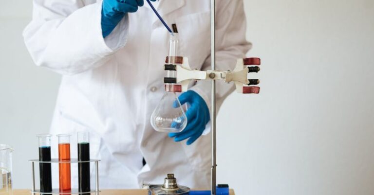 Conduct - Crop of unrecognizable scientist wearing lab coat and gloves and inserting pipette into empty flask mounted on ring stand while working in laboratory